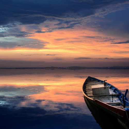 an image of an empty rowboat that is on the waters as the sun sets
