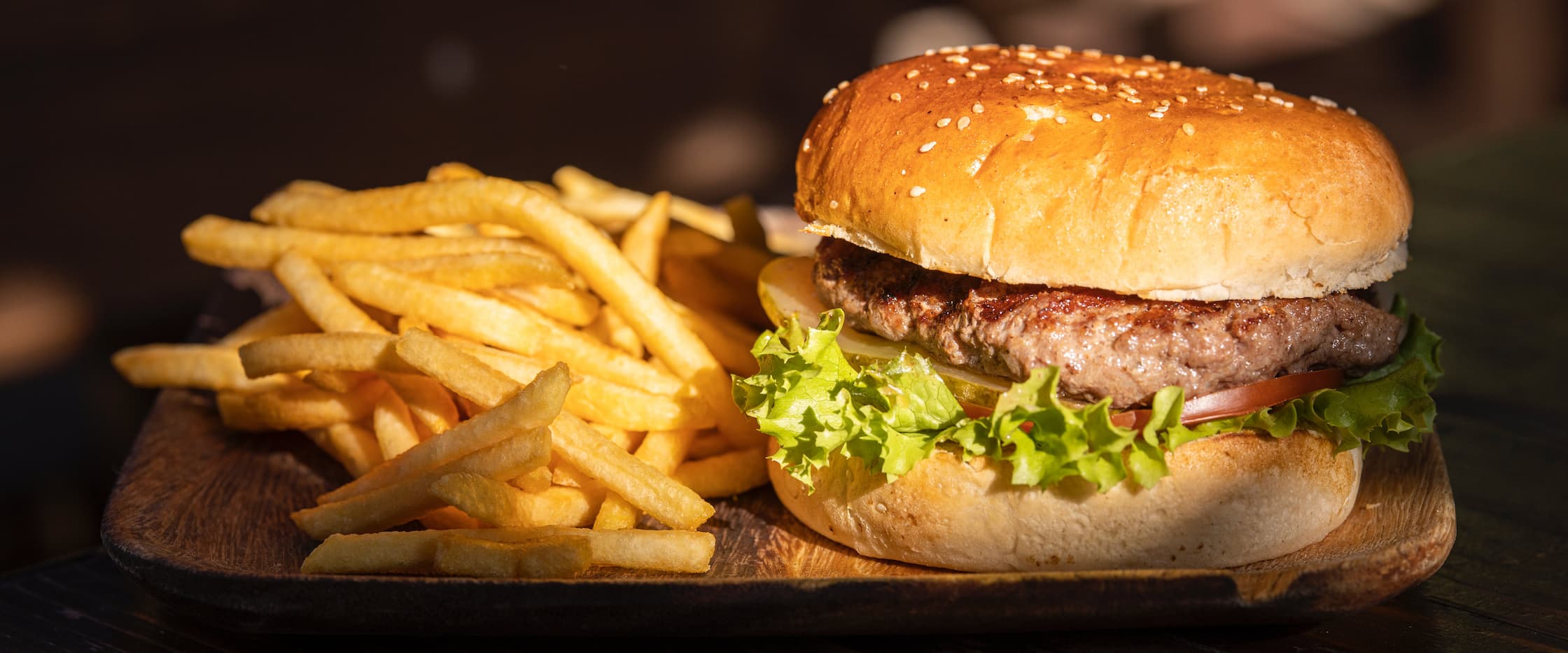 A burger with fries on the side and sunlight shining in on it.